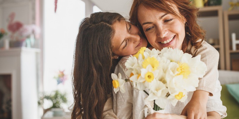 Mother looking at flowers, daughter hugging mom from behind